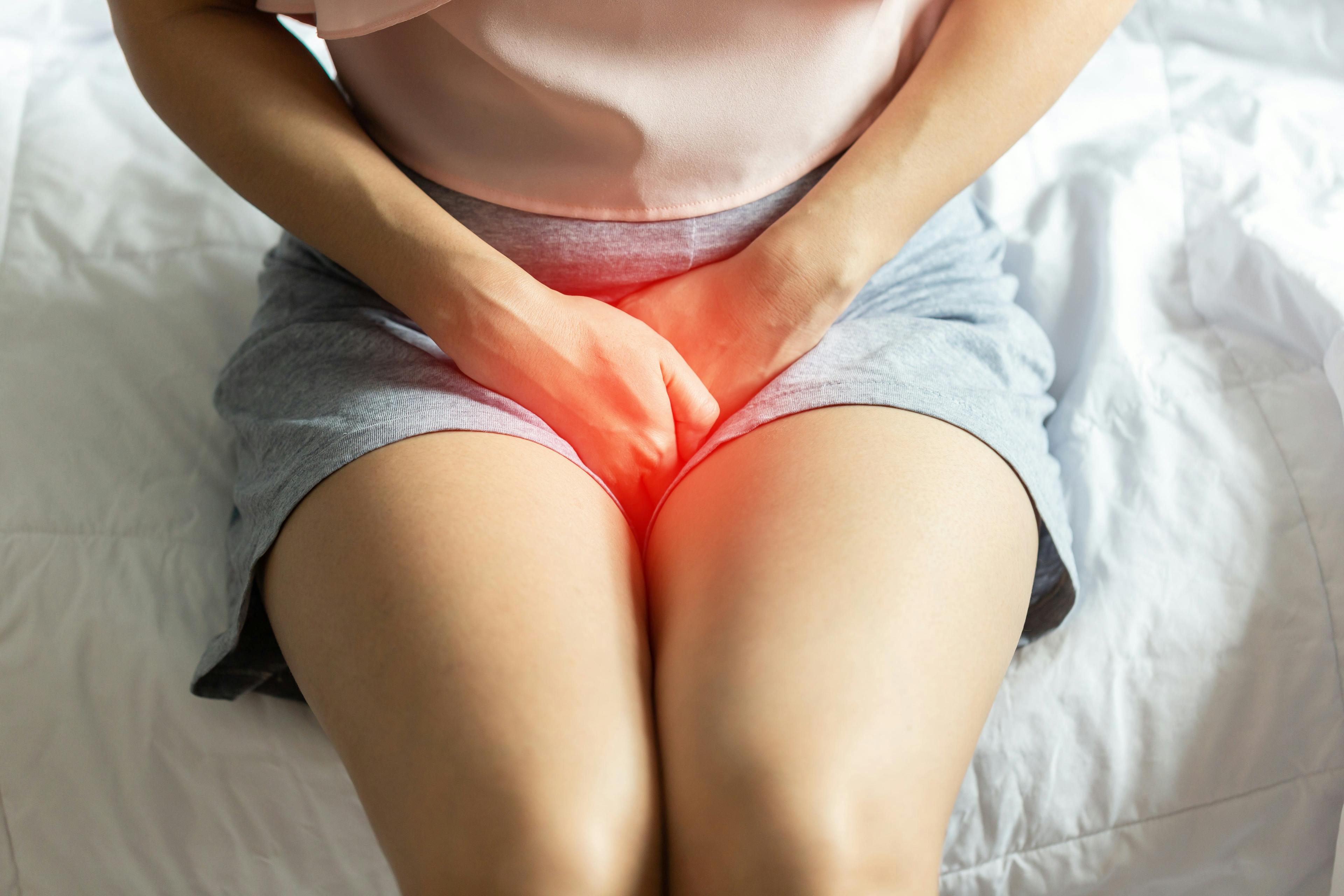 A woman sitting on her bed experiencing pelvic pain (highlighted in red) due to a UTI. 